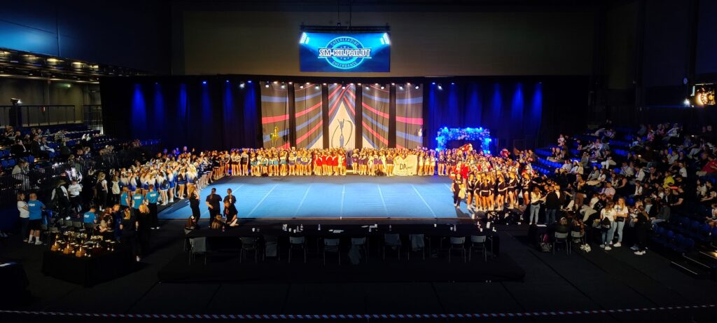 Pimeässä hallissa valokeilat permannolle, jonka reunoilla on ryhmittyneenä cheerleading-joukkueita
